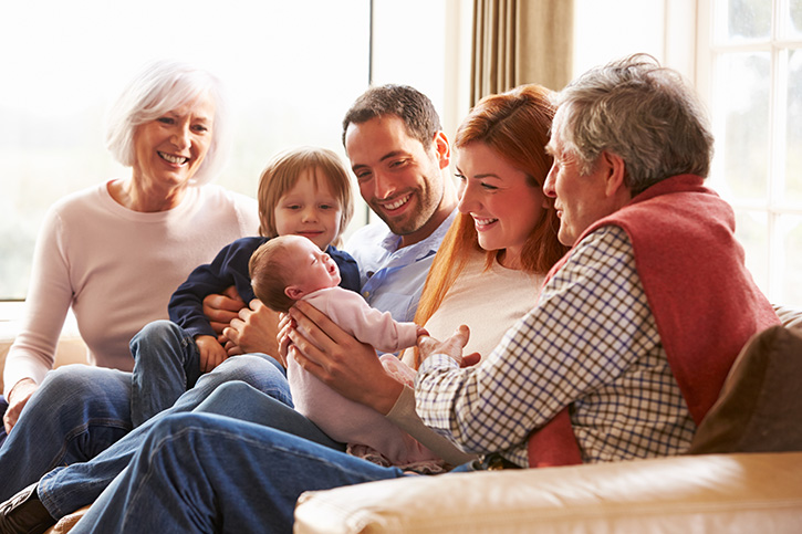 Multi Generation Family Sitting On Sofa With Newborn Baby Multigenerational Family